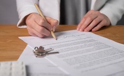 Property keys on desk with real estate contract and agent signing agreement